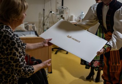Artysta Chóru w kostiumie łowickim wręczający kalendarz 2026 pacjentce Kliniki "Budzik" dla dorosłych