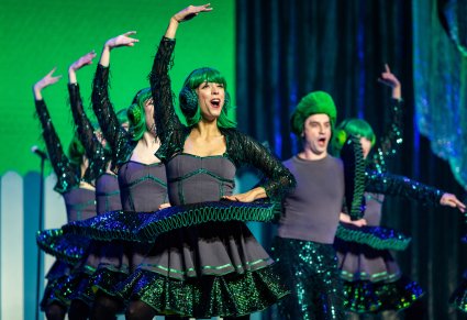 Grupa Artystów grających postacie kół w zielonych kostiumach podczas wykonywania choreografii tanecznej