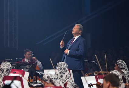 Zbliżenie na Dyrygenta trzymającego w ręku batutę. Widoczna część Artystów Orkiestry w kostiumach wilanowskich