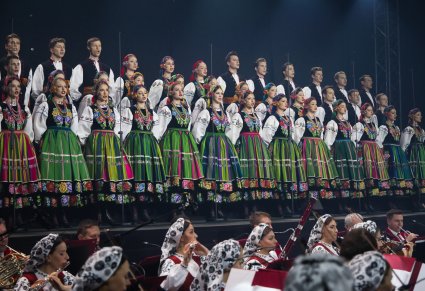 Na scenie widoczna część Artystów Chóru w kostiumach łowickich, niżej Artyści Orkiestry w kostiumach wilanowskich