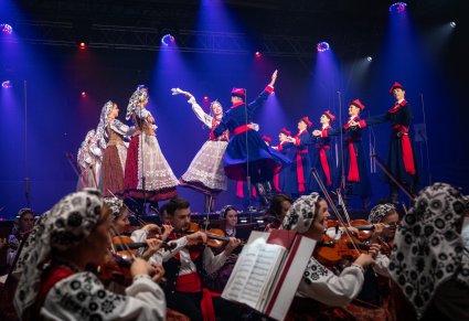 Na scenie Artyści w kostiumach wilanowskich w trakcie wykonywania choreografii tanecznej, niżej część orkiestry w kostiumach wilanowskich
