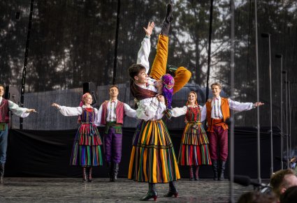 Na środku sceny para Artystów Baletu wykonująca imponujące figury taneczna, w tle sceny widoczna część Artystów w kostiumach opoczyńskich