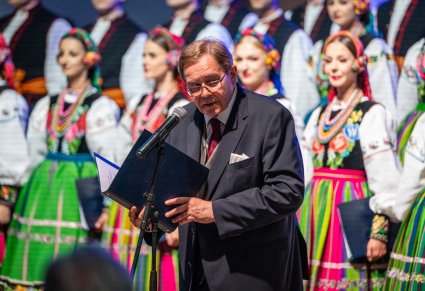 Na pierwszym planie Mirosław Ziomek zwrócony ku publiczności wygłaszający przemowę do mikrofonu