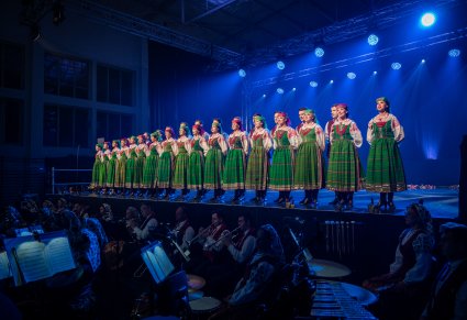 Chór w kostiumach kurpiowskich podczas występu, widoczna obok orkiestra