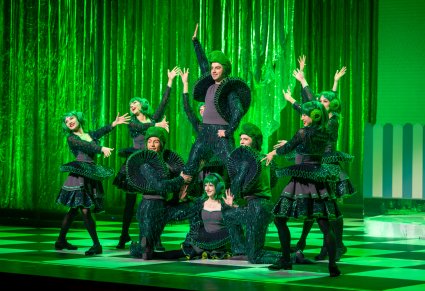 Grupa postaci kół w zielonych kostiumach podczas wykonywania choreografii tanecznej