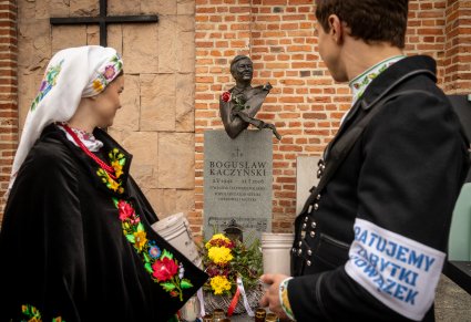 Para Artystów w kostiumach kocierzewskich na tle grobu z popiersiem Bogusława Kaczyńskiego