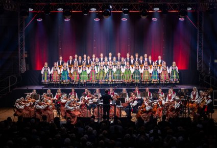Dyrygent zwrócony w stronę orkiestry i chóru. Orkiestra w kostiumach wilanowskich a chór w kostiumach łowickich