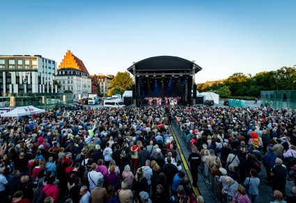 Widok na całą scenę wraz z publicznością wrocławską. Na scenie Artyści Baletu w trakcie wykonywania choreografii tanecznej, w tle Orkiestra w kostiumach wilanowskich
