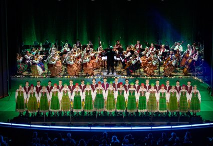 Na pierwszym planie Artyści Chóru w kostiumach kurpiowskich, ustawieni w dwurzędzie, Artystki stoją przed Artystami. Na