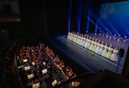 Na scenie Artyści chóru w kostiumach stylowych z końca XIX w., niżej orkiestra w kostiumach wilanowskich