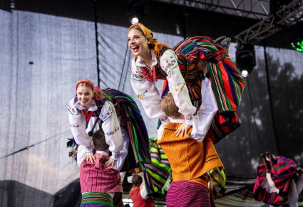 Partner podnoszący w górę swoją partnerkę, wykonując choreografię taneczną. Artyści w kostiumach opoczyńskich