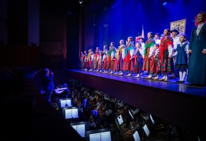 Orkiestron z Muzykami a na scenie Artyści w kostiumach ludowych podczas spektaklu