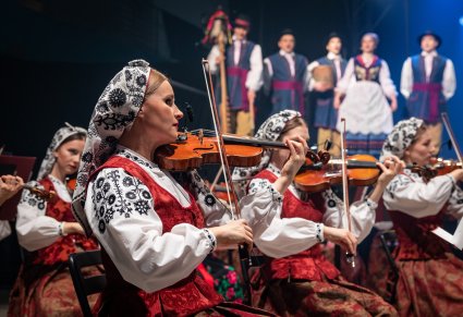 Na pierwszym planie część orkiestry smyczkowej, w tle na scenie Artyści w kostiumach kaszubskich