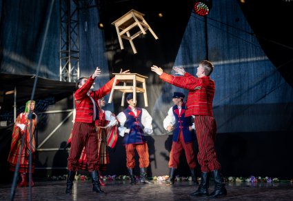 Artyści w trakcie przerzucania sobie drewnianych stołków jako elementu choreografii tanecznej. Artyści w kostiumach sieradzkich