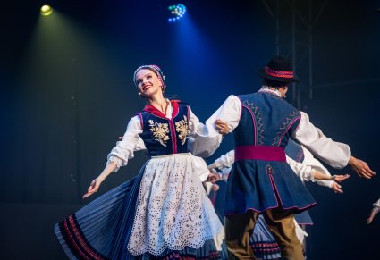 Para Artystów w kostiumach kaszubskich w trakcie wykonywania choreografii tanecznej na scenie