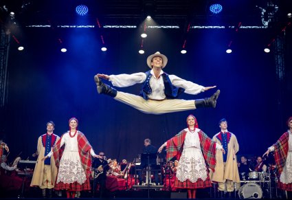 Na scenie Artyści Baletu w kostiumach łańcuckich w trakcie wykonywania choreografii tanecznej. Na pierwszym planie Artysta Baletu wykonujący sznurek w górze