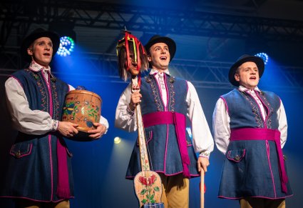 Trzech Artystów w kostiumach kaszubskich w trakcie śpiewu, widoczne instrumenty kaszubskie