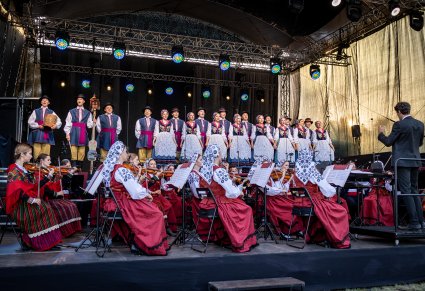 Na pierwszym planie orkiestra z dyrygentem a na drugim planie chór na scenie w kostiumach kaszubskich
