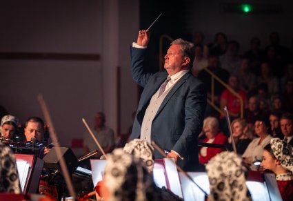Zbliżenie na dyrektora podczas koncertu, widoczna też widownia i orkiestra