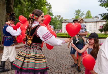 Para Artystów w kostiumach ludowych rozdająca balony dzieciom na Pikniku Rodzinnym, w tle widoczny Pałac w Karolinie