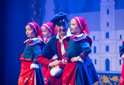 Artysta z młodszymi dziewczynkami w kostiumach kujawskich w trakcie odgrywania sceny w spektaklu