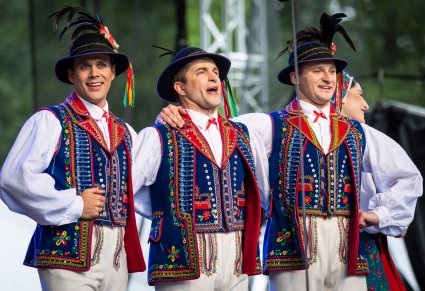 Trzech artystów w kostiumach limanowskich śpiewa na scenie