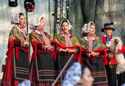 Artystki w kostiumach wielkopolskich śpiewają a obok nich koźlarz gra na koźle