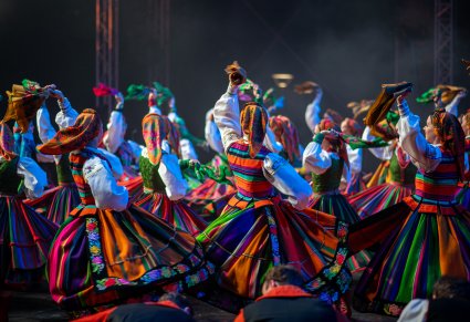 Artystki w kostiumach łowickich tańczą w ruchu wirowym na scenie