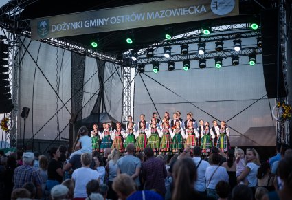 Chór w kostiumach łowickich śpiewa pieśni a przed nimi zgromadzona Publiczność