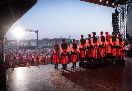 Chór w kostiumach łowickich śpiewa pieśni a przed nimi zgromadzona Publiczność