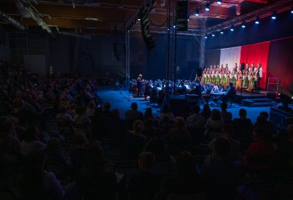 Chór w kostiumach łowickich śpiewa pieśni a przed nimi zgromadzona Publiczność