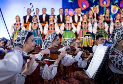 Zbliżenie na skrzypaczki a w tle widać chór w kostiumach łowickich