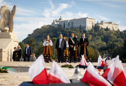 Przedstawiciele Mazowsza, dyrektor, zastępca burmistrza Cassino i sekretarz Marszałka Województwa Mazowieckiego stoją przed pomnikiem a na pierwszym planie flagi Polski