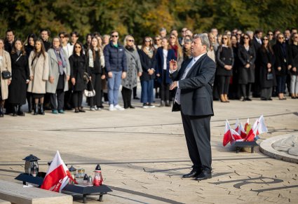 Dyrektor Jacek Boniecki dyryguje chórem a w tle widać zgromadzonych uczestników wydarzenia