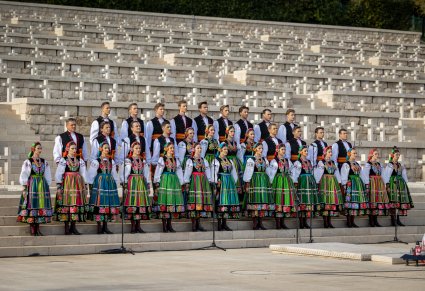 Chór w kostiumach łowickich stoi przed grobami żołnierzy i śpiewa