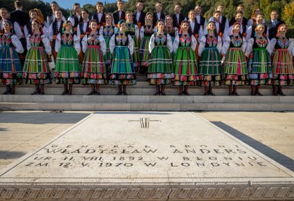 Chór Mazowsza w kostiumach łowickich przed płytą upamiętniającą Generała Władysława Andersa