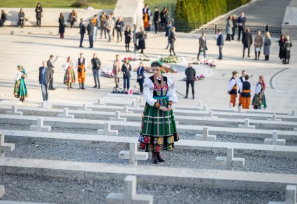 Artystka Mazowsza w kostiumie łowickim stoi przed jednym z grobów