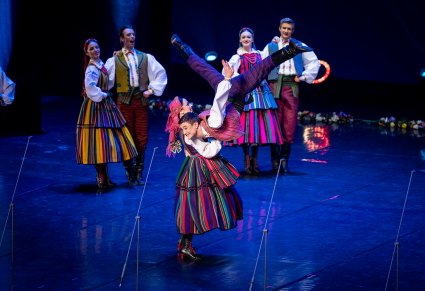 Na pierwszym planie para Artystów w kostiumie opoczyńskim w trakcie wykonywania imponujących figur tanecznych na scenie