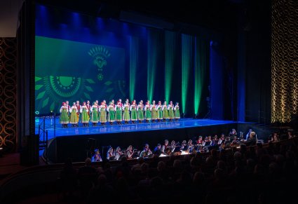 Na scenie chór w kostiumach kurpiowskich z widoczną orkiestrą w kostiumach wilanowskich