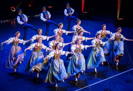 Na pierwszym planie Artystki w kostiumach pszczyńskich w trakcie śpiewu i wykonywania choreografii tanecznej