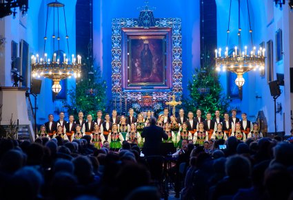 Na pierwszym planie Dyrektor Jacek Boniecki zwrócony w stronę orkiestry i Artystów z Chóru, widoczna część zaciemnionej publiczności. Artyści przed Ołtarzem są pięknie oświetleni