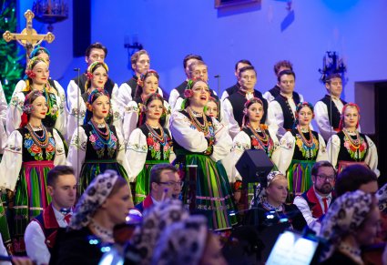 Na pierwszym planie Solistka a za nią Artyści chóru w kostiumach łowickich