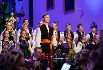 Na pierwszym planie Solista a za nim Artyści chóru w kostiumach łowickich