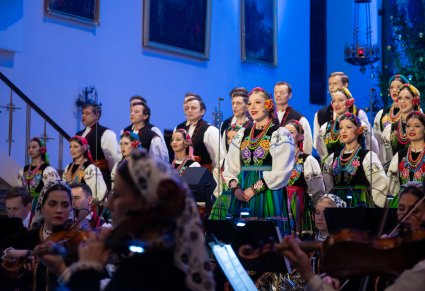 Na pierwszym planie Solistka a za nią chór w kostiumie łowickim, widoczna mała część orkiestry