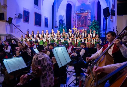 Na pierwszym planie część orkiestry a za nią na tle ołtarza rzędy Artystów chóru w kostiumach łowickich