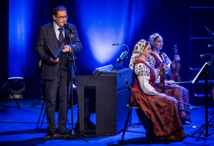 Mirosław Ziomek w trakcie wypowiedzi do mikrofonu, widoczne dwie skrzypaczki