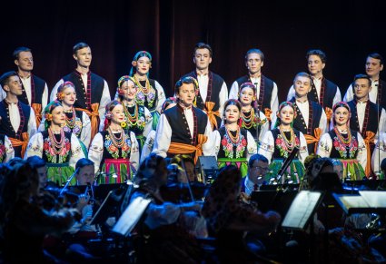 Na pierwszym planie Solista wraz z Chórem w kostiumach łowickich przed nimi Orkiestra