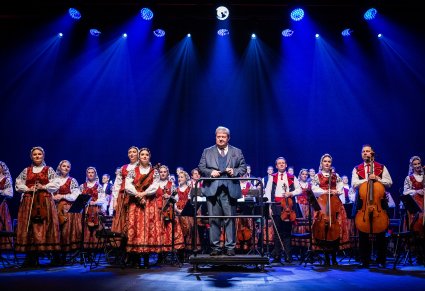 Dyrektor Jacek Boniecki zwrócony w stronę publiczności, za nim Orkiestra
