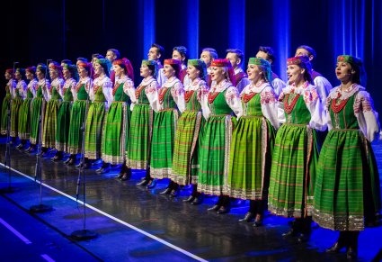 Artyści z chóru ustawieni w rzędach na scenie w kostiumach kurpiowskich