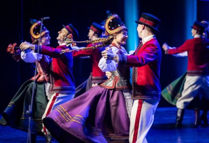 Uśmiechnięte pary Artystów w kostiumach kurpiowskich na scenie wykonujący choreografię taneczną